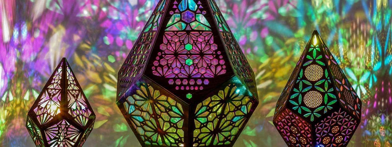 Three handcrafted geometric lamps projecting intricate coloured patterns across a wall.