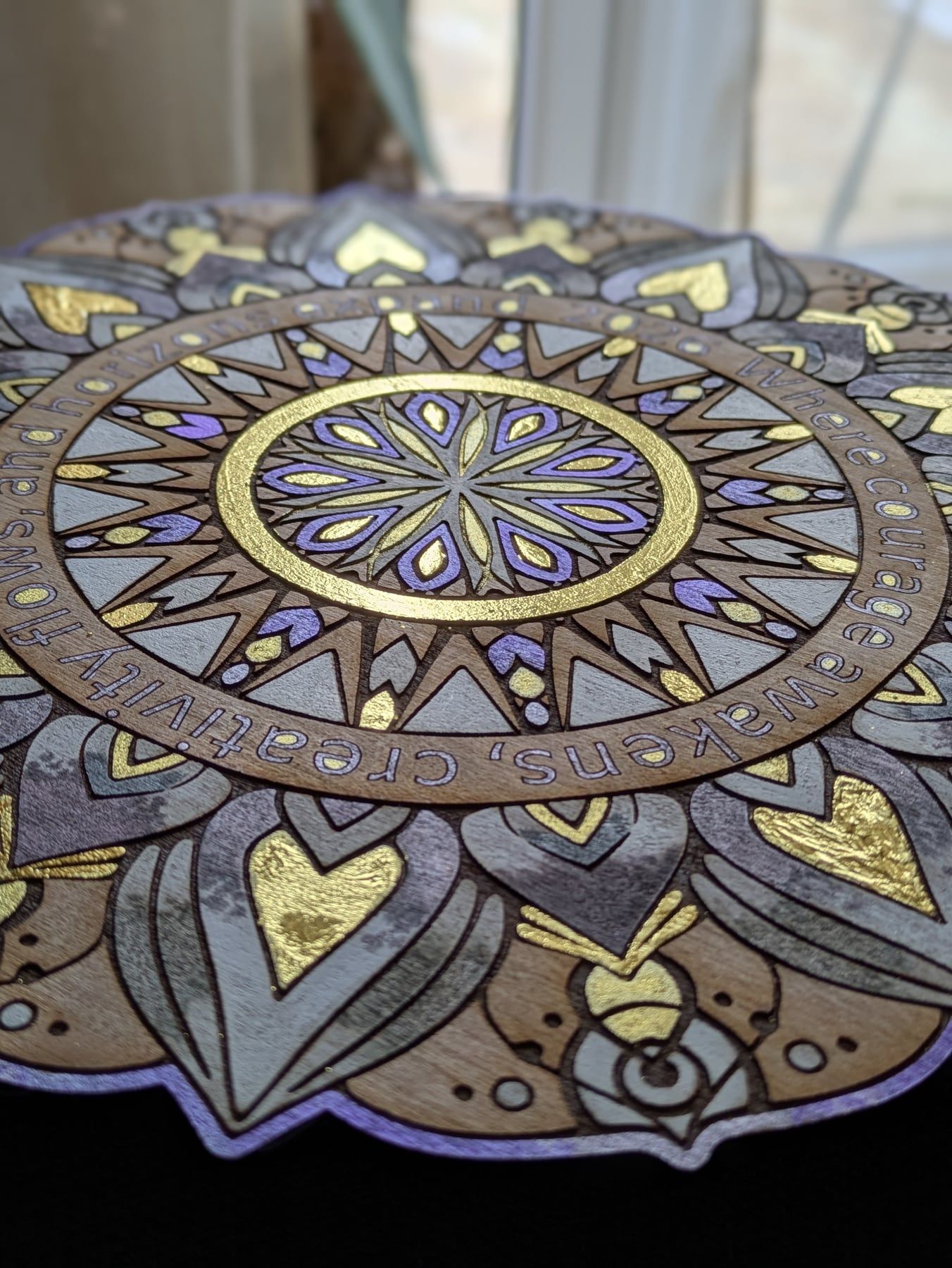 A gold leaf mandala in progress, its engraved ring reading words of intention.