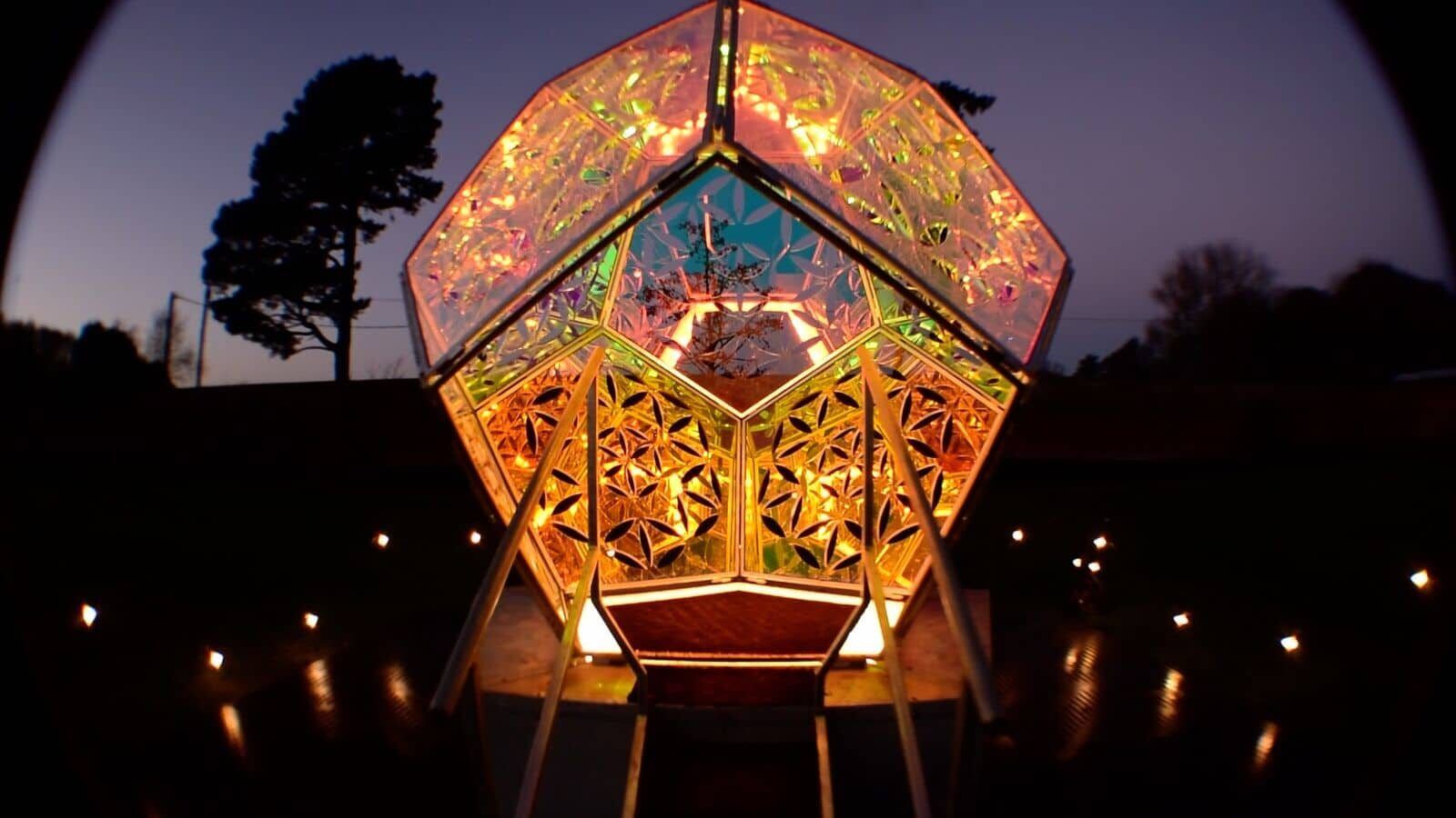 The Seed of Life dodecahedron glowing orange, green and pink against a dusk sky.