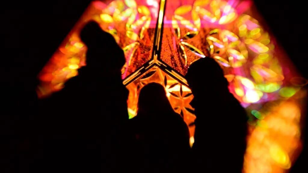 Three people silhouetted inside the Seed of Life sculpture, surrounded by projected orange and pink patterns.